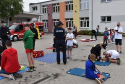 policjantka i strażacy uczą dzieci udzielania pierwszej pomocy na fantomach