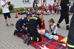 policjantka i strażacy uczą dzieci udzielania pierwszej pomocy na fantomach