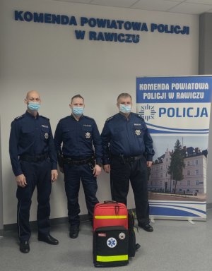 trzech policjantów na tle baneru KPP Rawicz oraz z walizką medyczną nr 2