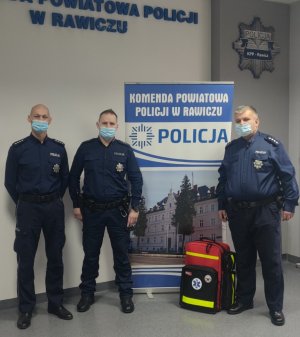 trzech policjantów na tle baneru KPP Rawicz oraz z walizką medyczną
